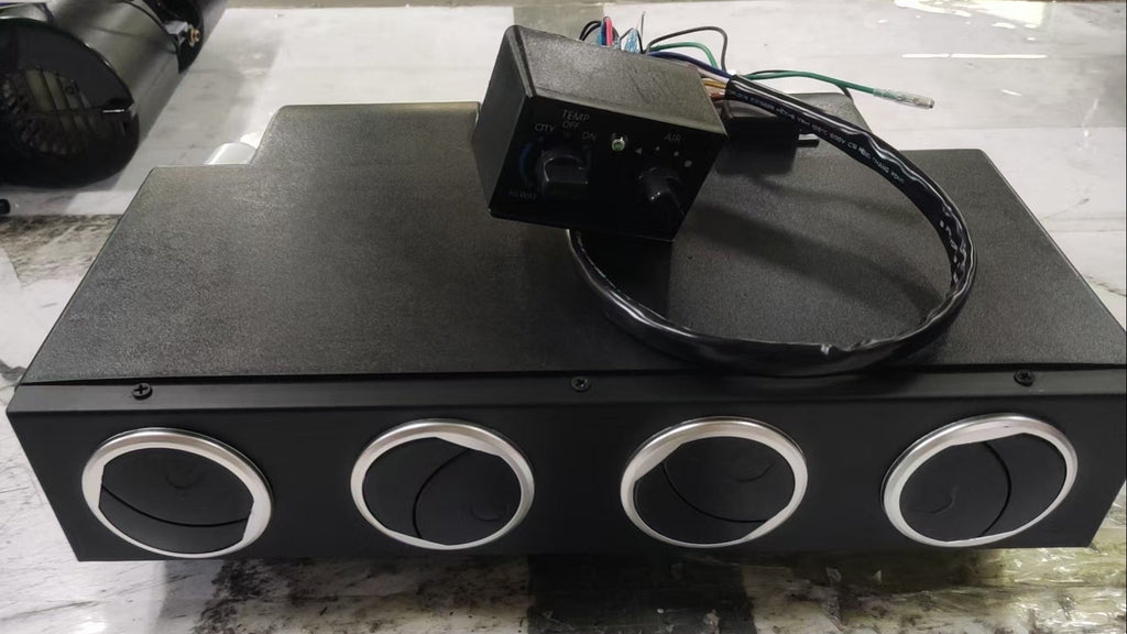 A black rectangular electronic control box with four circular silver-rimmed ports on the front, placed on a light gray marble-like surface. A small black wired control module sits on top of the unit.