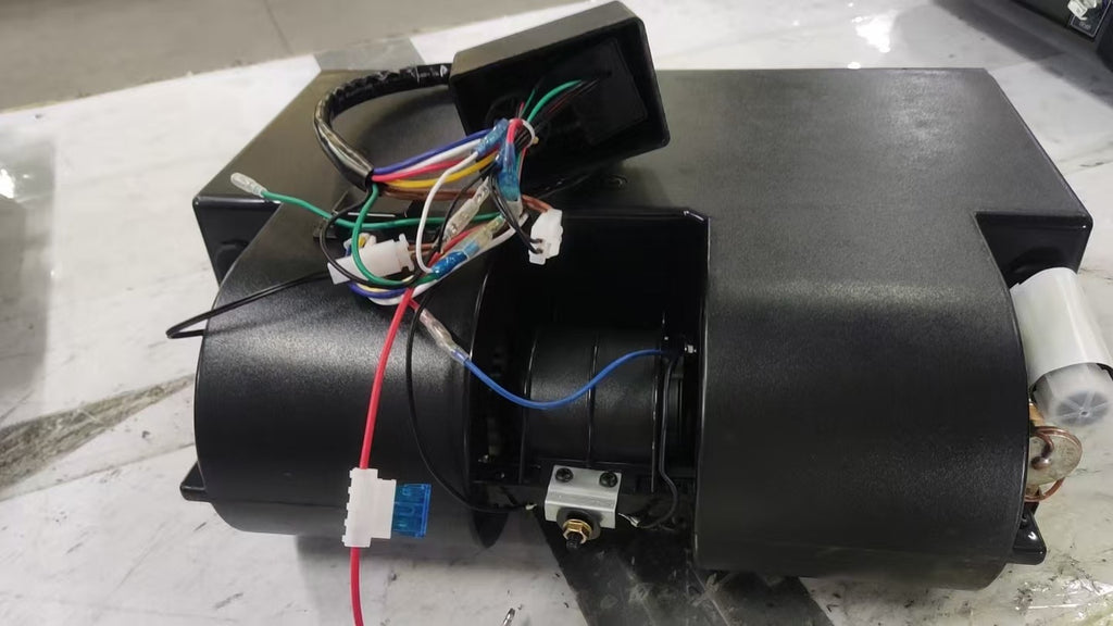 A black plastic mechanical component, with various colored wires connected to connectors and a small white cylindrical part visible on the right side, photographed on a light-colored floor.