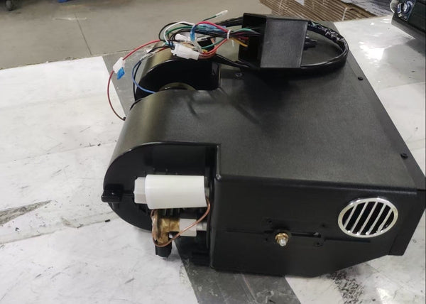 A black metal cooling component with attached wiring, photographed on a white workbench in a workshop setting.